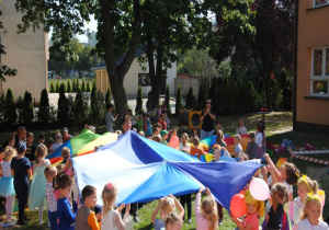 w ogrodzie dzieci bawia się chustami animacyjnymi w trzech grupach